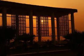 Photograph of a perforated screen colonnade backlit by a low orange sun.