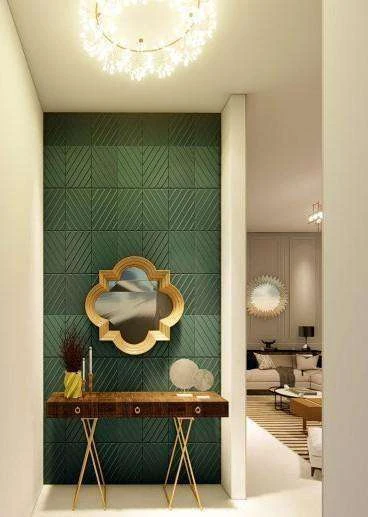 Entrance foyer with a hunter green three-dimensional panelled wall, a quatrefoil mirror above a slim brass-legged console and a chandelier.